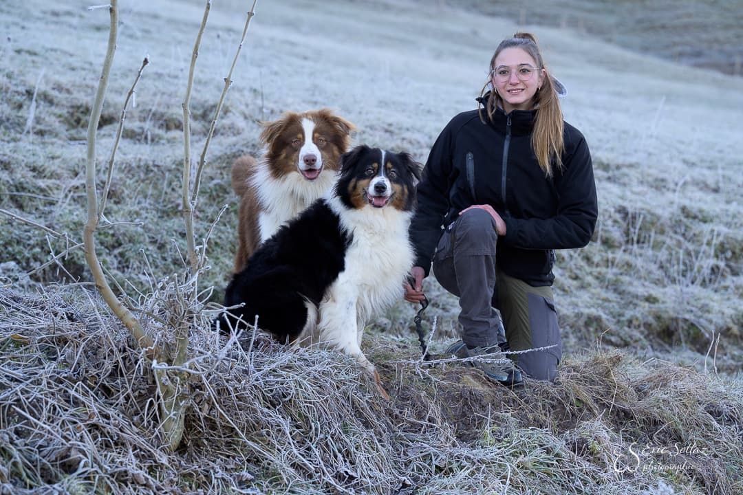 Une gardienne et deux chiens dans un pré givré au petit matin